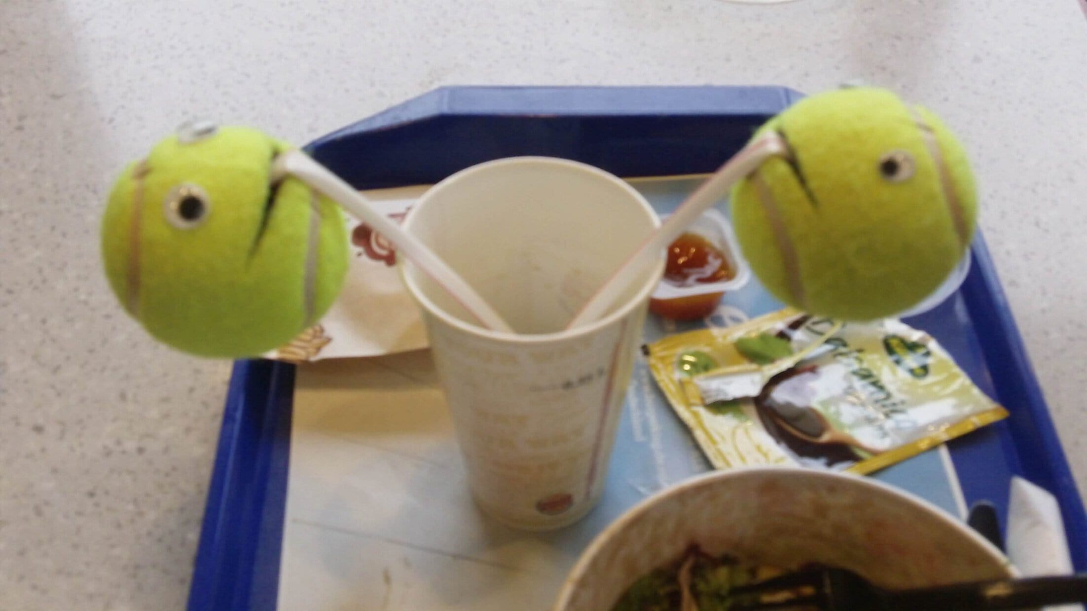 Zwei Bälle, die wie Ball-kun und Derp-kun aussehen, hängen an Strohhalmen in einem Becher.
