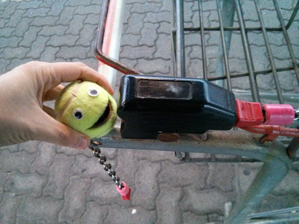Ball-kun, der lachende gelbe Ball, im Einkaufswagen mit Schlosskette.