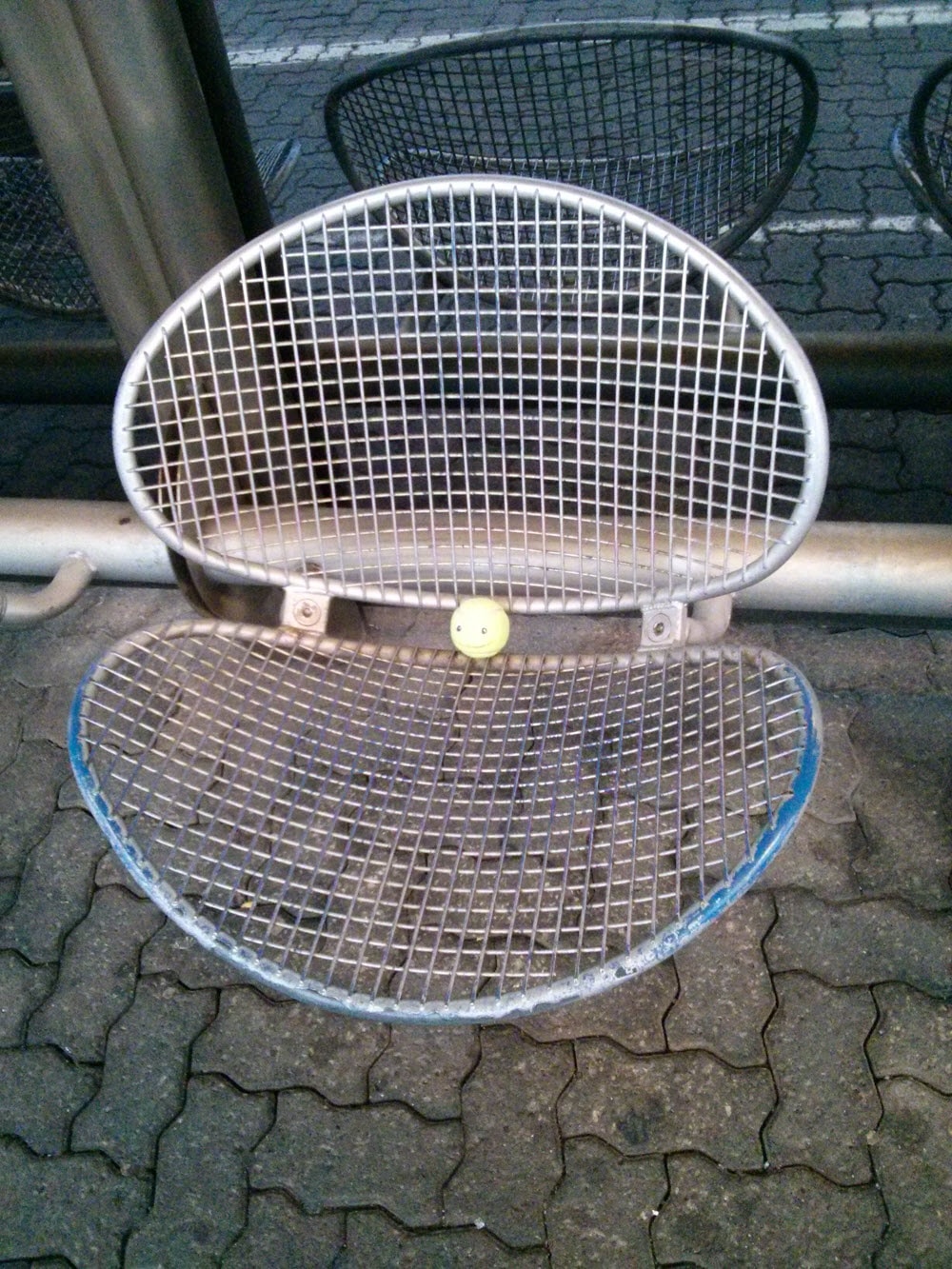 Metallischer Sitz mit Ball auf gepflastertem Boden.
