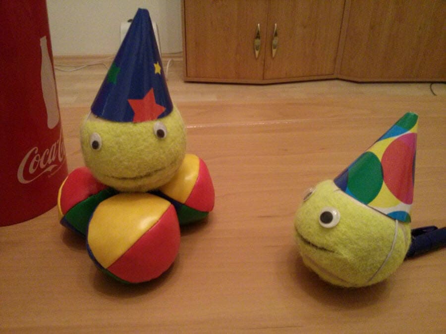 Zwei bunte Bälle mit Partyhüten und Augen auf einem Holztisch.