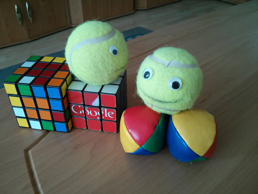 Zwei Bälle mit Augen, Rubik's Cube und Google-Logo auf Holz.