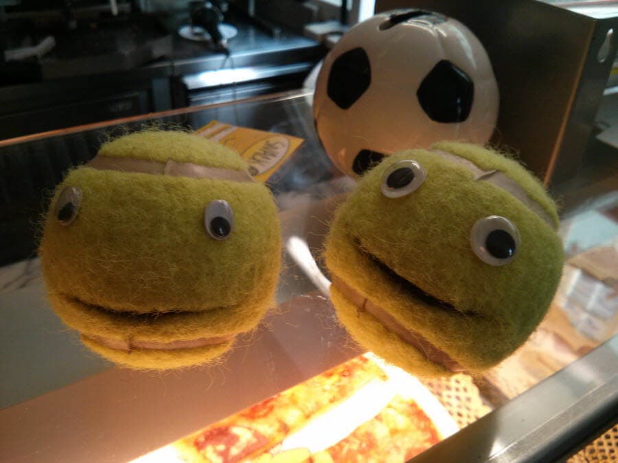 Zwei grüne Plüschbälle mit Augen und Mund, Fußball im Hintergrund.