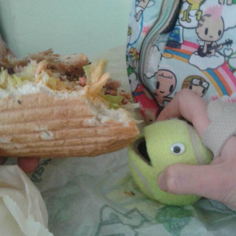Spielzeugball und Sandwich auf Tisch, bunte Tasche im Hintergrund.