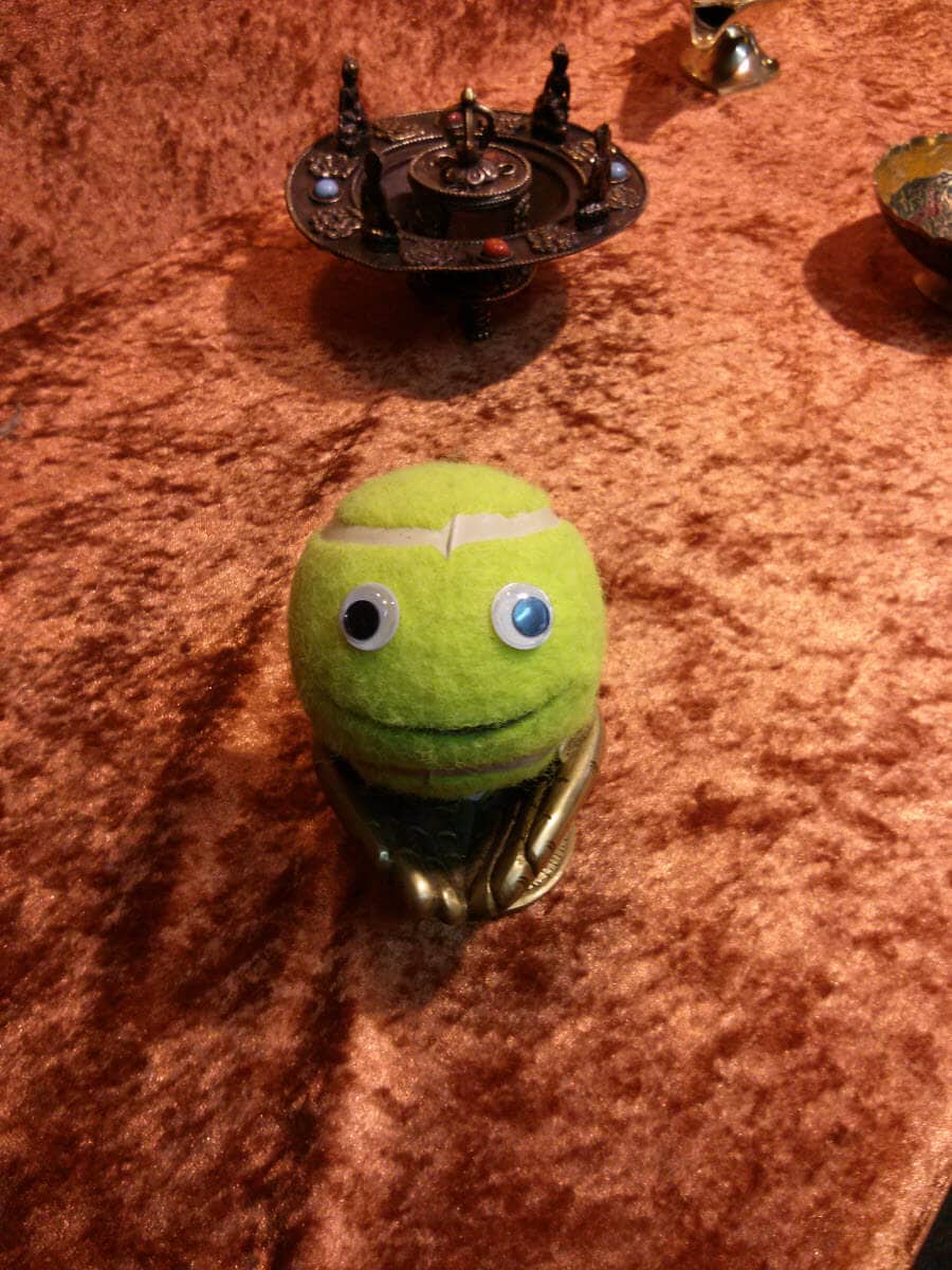 Ball-kun mit einem großen Auge und einem kleinen Auge, auf einem braunen Tisch.