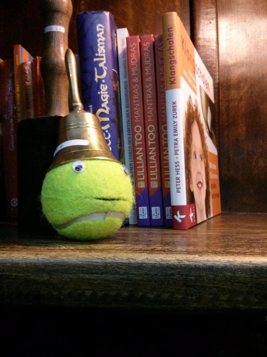 Grüner Ball mit Auge, an einer Schnur, neben Büchern auf Holzregal.
