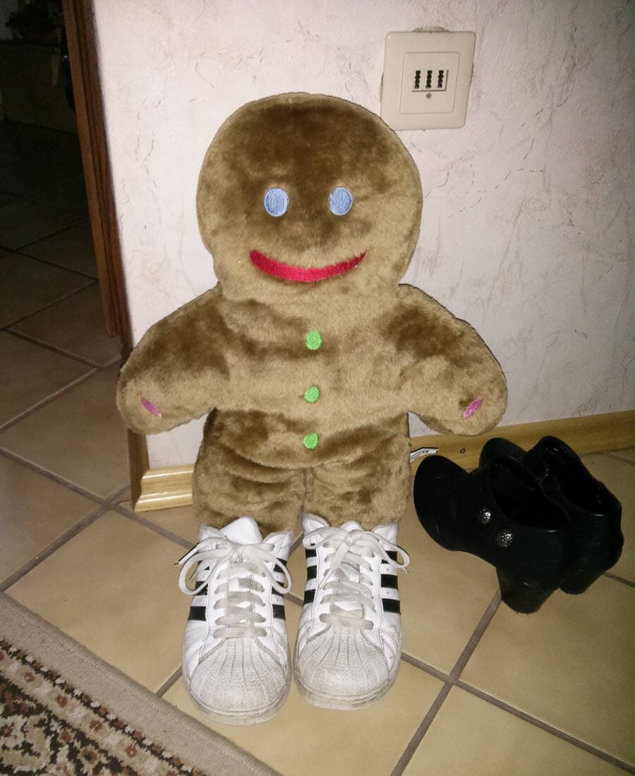 Lebkuchenmann trägt weiße Turnschuhe und steht neben schwarzen Schuhen.