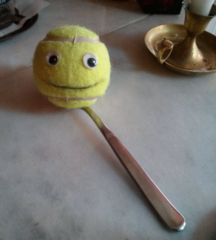 Tennisball mit Augen und Lächeln auf einem Löffel.