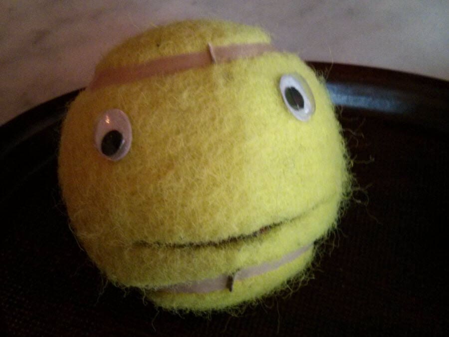 Gelber Ball mit Augen, Lächeln und Schleife, auf dunklem Hintergrund.