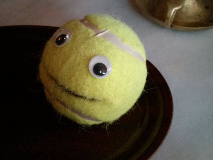 Tennisball mit Augen und Mund, auf dunklem Teller.