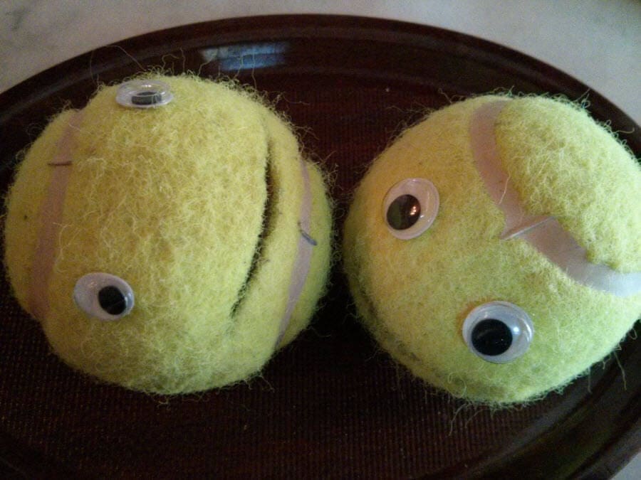 Zwei gelbe Tennisbälle mit künstlichen Augen und Gesichtsausdrücken.