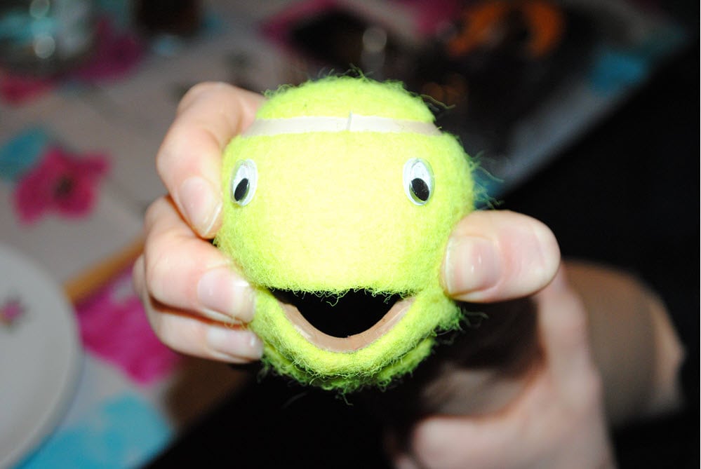 Hand hält einen grünen Ball mit Augen und lachendem Mund.